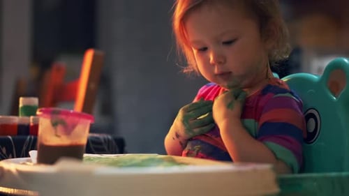 Baby and paints. Toddler girl plays with paints at home