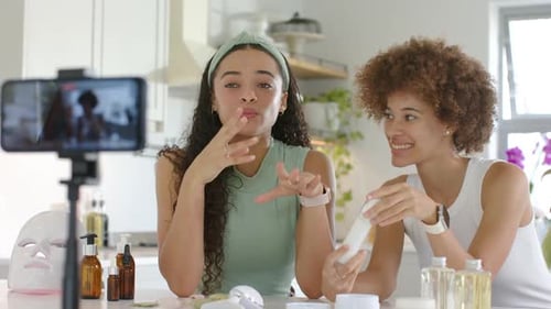 Dos mujeres filmando un teléfono de cuidado de la piel grabándolas, con la izquierda tocando la cara, el tubo de lectura a la derecha en la cocina