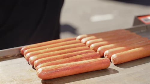 Hot Dogs Being Prepared on Grill Surface with Tongs During Cooking Process