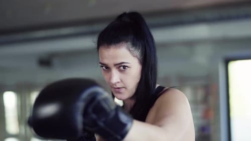 Young woman training with boxing gloves at the gym for fitness and health