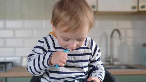 Child Eating in Kitchen with Blue Spoon