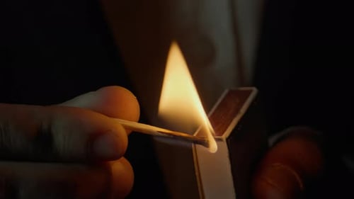 Finger griffig beleuchtetes Streichholz, herunterdrückendes Ende, Flamme auf festem dunklem Hintergrund, Nahaufnahme