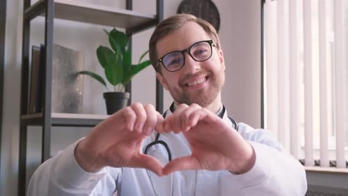Retrato de un joven médico general sonriente con uniforme médico blanco que muestra el corazón, la mano del amor