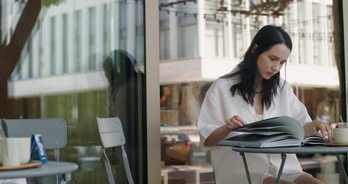 Young Woman Reading Book at Outdoor Cafe Table