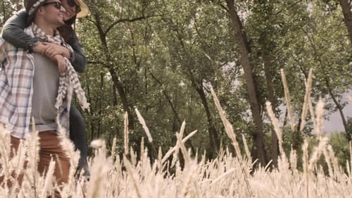 Romantic caucasian couple piggyback ride in a sunny field having fun together