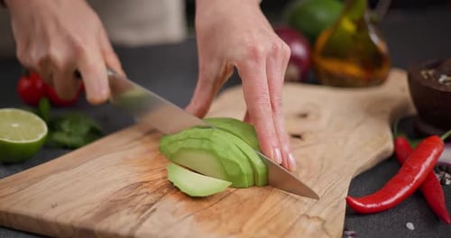 Woman Cutting Slicing Fresh Green Avocado Fruit with Knife on a Wooden Board at Domestic Kitchen