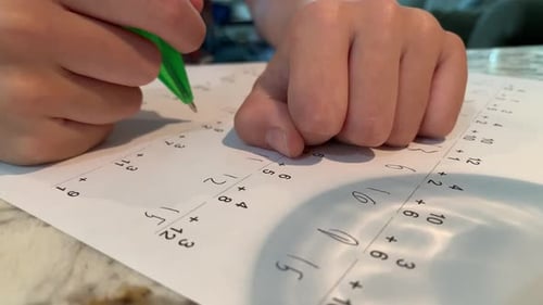 Elementary aged student doing math (addition problems) on a practice worksheet.