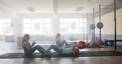 Unaltered diverse women group training in pairs with medicine balls at gym, slow motion, copy space