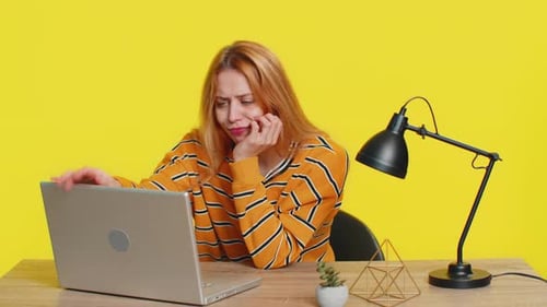 Frustrated Woman Working at Laptop on Yellow Background