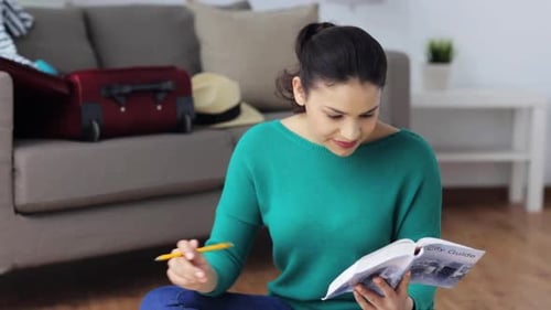 Happy young woman prepares for her travel adventure at home with city guide