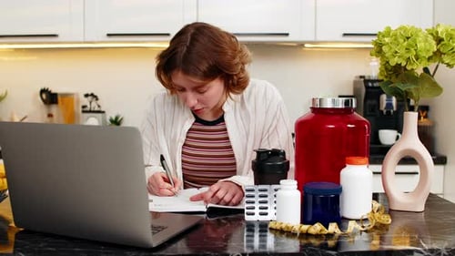 Young Woman Writing Fitness Supplement List in Notebook for Diet Plan and Healthy Workout Nutrition