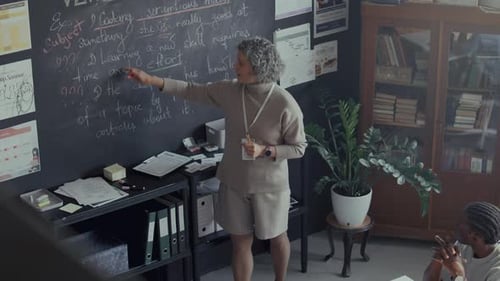 Teacher Giving Lesson at Chalkboard in Classroom