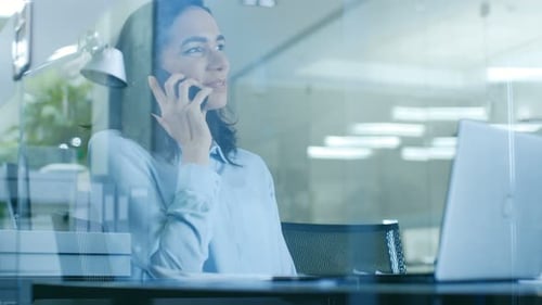 Beautiful Female Office Worker Makes a Client Call and Talks on the Mobile Phone while Sitting at H