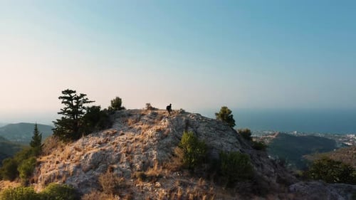 Man climbs on the top of the mountain. Marvelous mountain range view at sunset with city and sea in