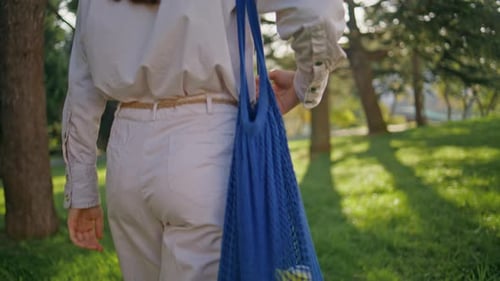 Mujer consciente que lleva una bolsa de compras ecológica reutilizable en verde, Sunny Park, primer plano