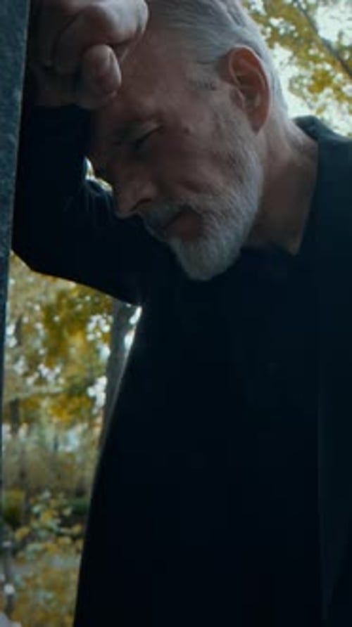 Sorrowful Man Overcome by Loss Leaning on Gravestone in Cemetery