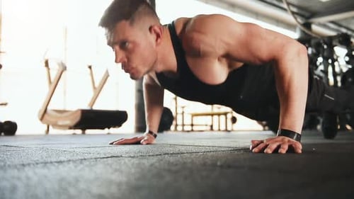 Young sportive strong man in black wear doing push-ups in gym