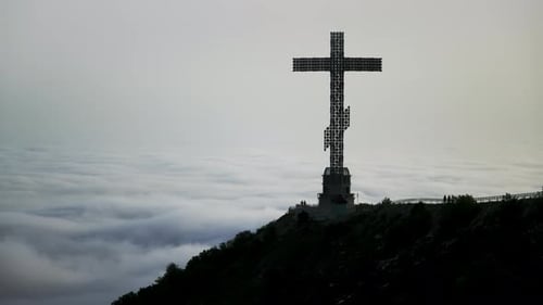 Massive Christian Cross Towers on Mountain with Clouds Drifting Beneath It in Timelapse Blend of