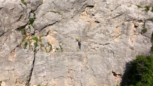 Climber rappelling down cliff with helmet and backpack