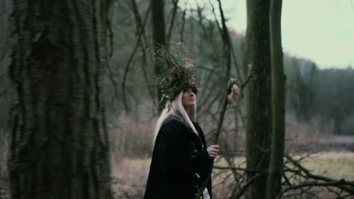 Wild girl with natural crown and skull on stick walking in forest, side view