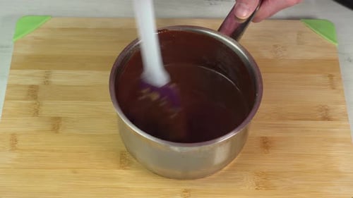Rühre heiße Schokolade in einem Topf mit einem Küchenspatel von Hand um, um ein Dessert zuzubereiten.
Kochen