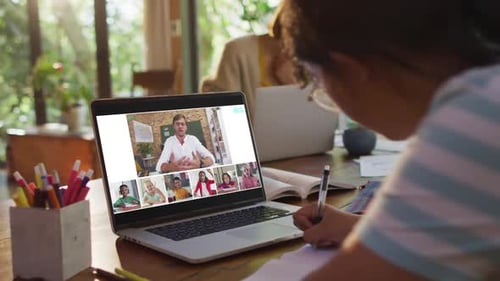 Schoolgirl using laptop for online lesson at home, with diverse teacher and class on screen