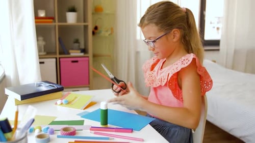 Childhood, Creativity And Hobby Concept - Creative Girl Cutting Color Paper With Scissors At Home