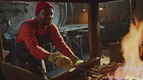Black Man Heating Metal Billet in Forge Fire at Work in Smithy