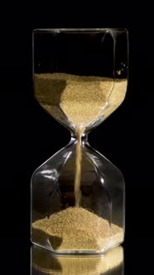 Gold Sand Flowing Through Hourglass on Black