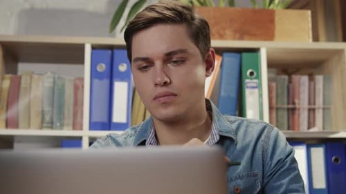 Gut aussehender intelligenter junger Büroleiter, der denkt und auf einen Monitor schaut, der auf einem modernen Laptop arbeitet