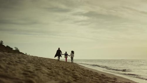 Family running on beach enjoying summer vacation near ocean at sunset