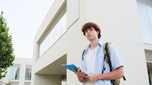 Young Male Student Walking and Reading at University Campus
