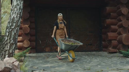Woman Pushing Wheelbarrow with Leaves in Rural Setting