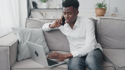 Man Working on Laptop and Talking on Phone
