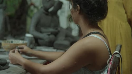 Woman sculpting clay figure at a pottery workshop, focused and engaged in her craft