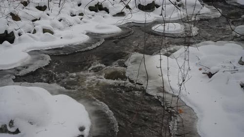 Tauwetter im frühen Frühling mit fließendem Bach zwischen schneebedeckten Ufern