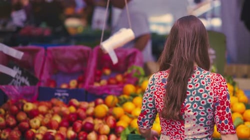 woman with brown hair going towards the fruit stand at the fair to choose one of them. back view