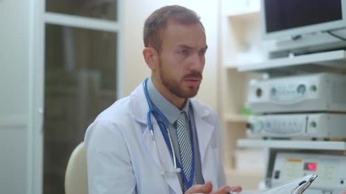 Focused Doctor Consults Patient, Writing on Clipboard