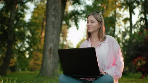 Junge Dame arbeitet im Freien mit warmem Lächeln und nachdenklichem Gesichtsausdruck am Laptop