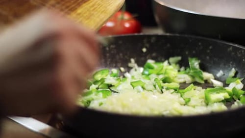 Scraping chopped white onions with a knife from a wooden chopping board into a black frying pan with