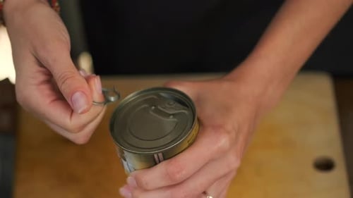 female hands opening a tin can with a ring on the lid unsuccessfully coming off, top view, close-up