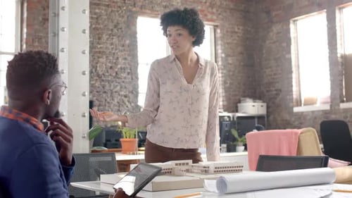 Focused diverse architect colleagues discussing work with building model in office in slow motion