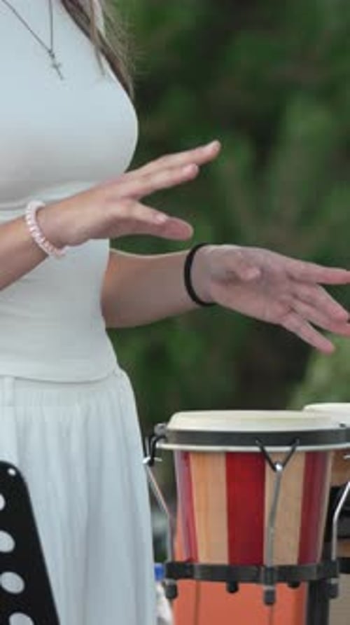 Woman Plays Bongos Outside, Demonstrating Musical Rhythm