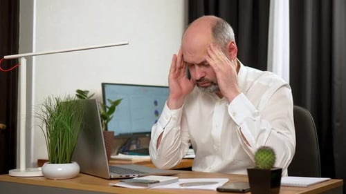 Man Massaging Temples at Desk with Laptop
