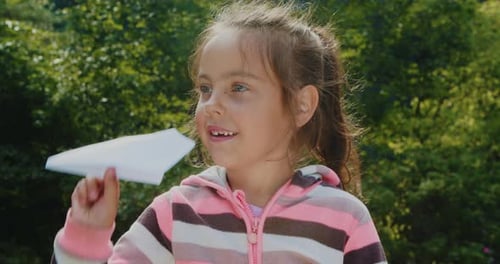 Happy Girl Holding a Paper Airplane Outside