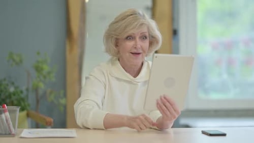 Senior Woman Celebrates Using Tablet at Table Indoors