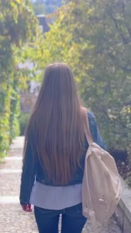 Woman with Backpack Walks Down Path in Park