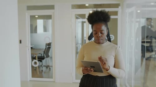 African American Businesswoman Walking through Office Corridor and Using Tablet