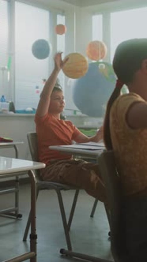 Elementary School Students Sitting at the Desks Raising Hands to Provide Correct Answer
