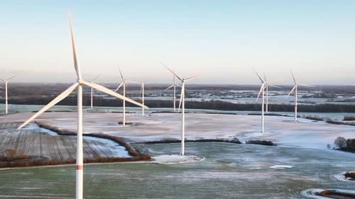 Aerial footage of wind turbines gracefully spin, one up close with more wind turbines in the distanc